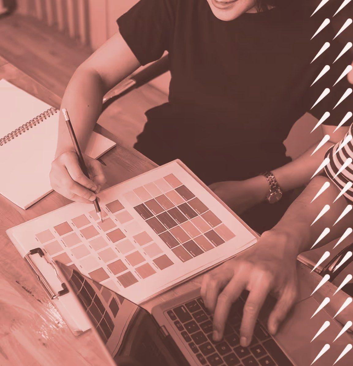 Designer marking up a sheet of colour swatches beside a laptop, in a coral duotone with Dynastic droplet marks